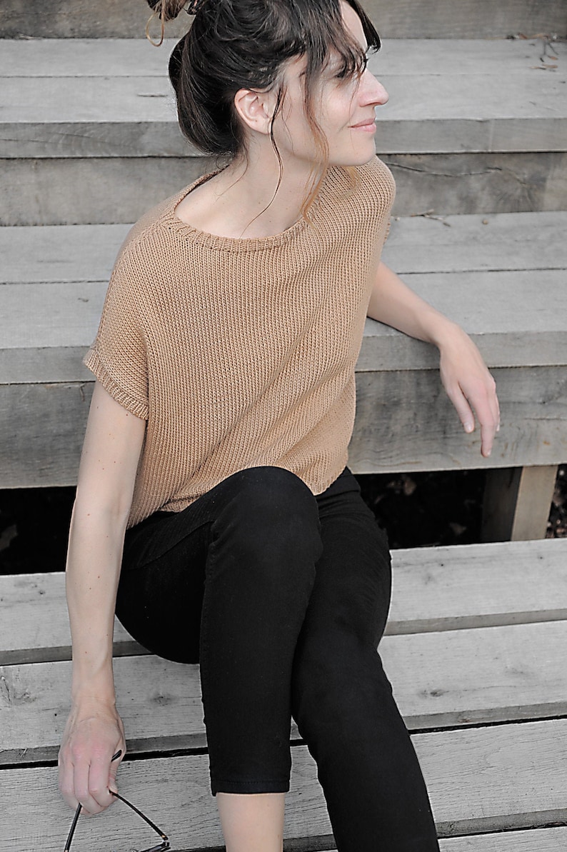 Pu&ograve; includere: Una donna con un maglione di lana marrone e pantaloni neri &egrave; seduta su gradini di legno.