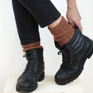 Pode incluir: Um par de meias de l&atilde; marrons at&eacute; o tornozelo, usadas com botas pretas de couro com cadar&ccedil;os. As botas s&atilde;o usadas com cal&ccedil;as de ganga pretas.