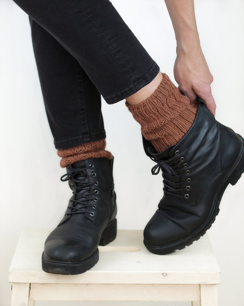 Pode incluir: Um par de meias de l&atilde; marrons at&eacute; o tornozelo, usadas com botas pretas de couro com cadar&ccedil;os. As botas s&atilde;o usadas com cal&ccedil;as de ganga pretas.