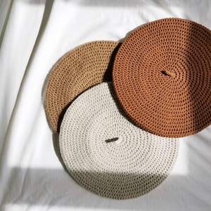 May include: Three crocheted round coasters in beige, light gray, and brown. The coasters are stacked on top of each other.