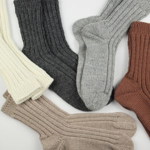 Pode incluir: Quatro pares de meias de malha em diferentes cores: bege, cinza, marrom e branco. As meias est&atilde;o dobradas e dispostas sobre um fundo branco.