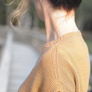 Pu&ograve; includere: Primo piano di una maglia a maniche corte. La maglia &egrave; di colore marrone chiaro e ha un motivo a maglia testurizzato.