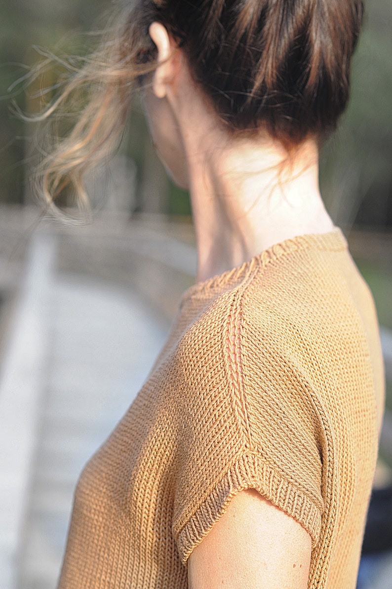 Pu&ograve; includere: Primo piano di una maglia a maniche corte. La maglia &egrave; di colore marrone chiaro e ha un motivo a maglia testurizzato.