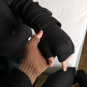 以下が含まれることがあります： 指なし手袋のペア、1つは茶色、もう1つは黒で、2つの手で一緒に持たれています。手袋は編んであり、質感のあるパターンがあります。