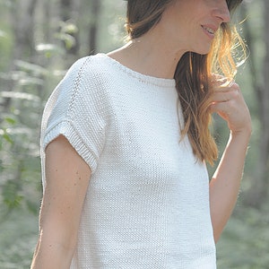 Pu&ograve; includere: Un top bianco lavorato a maglia con maniche corte e scollo rotondo. Il top &egrave; realizzato in un tessuto leggero e ha una vestibilit&agrave; rilassata. La modella indossa un cappello nero.