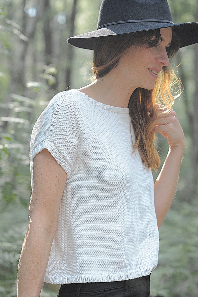 Pu&ograve; includere: Un top bianco lavorato a maglia con maniche corte e scollo rotondo. Il top &egrave; realizzato in un tessuto leggero e ha una vestibilit&agrave; rilassata. La modella indossa un cappello nero.
