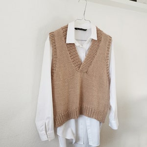 May include: A brown knitted vest with a V-neck and a white button-down shirt underneath.