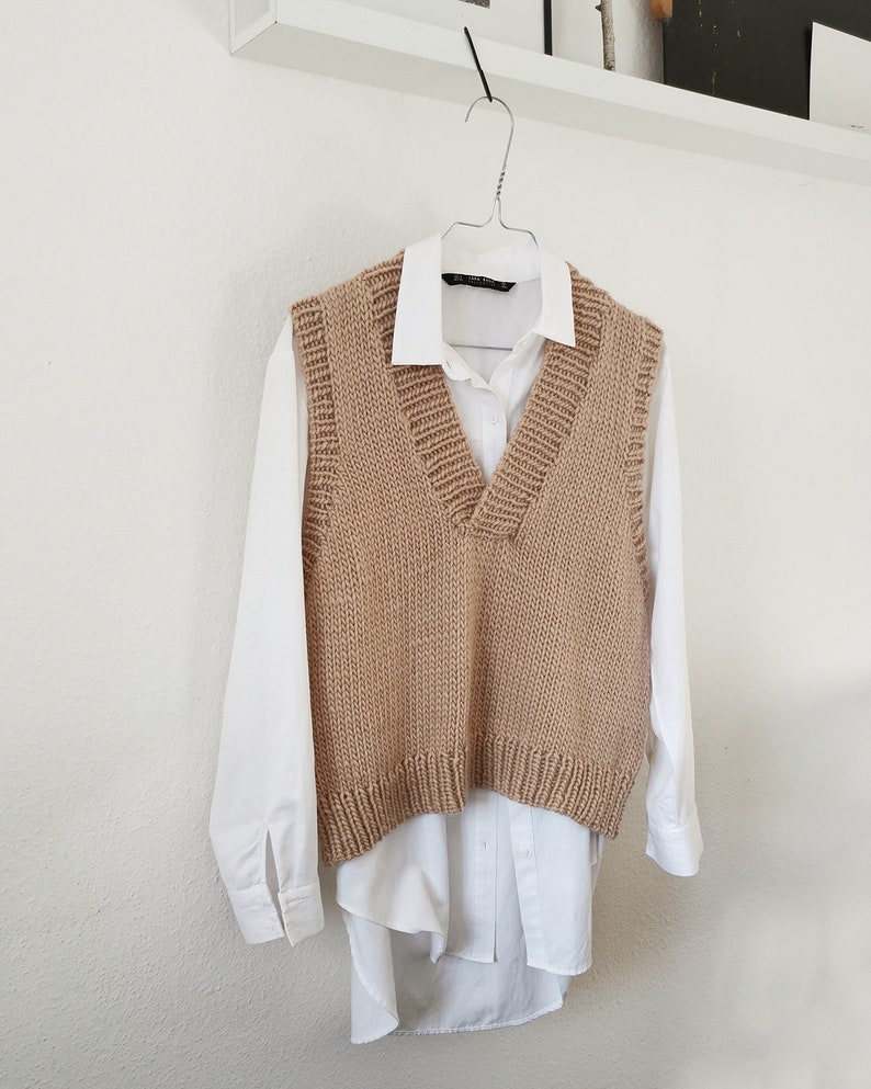 May include: A brown knitted vest with a V-neck and a white button-down shirt underneath.
