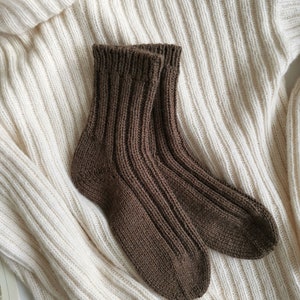 May include: A pair of brown knitted socks on a white knitted sweater. The socks are ribbed and have a simple design.