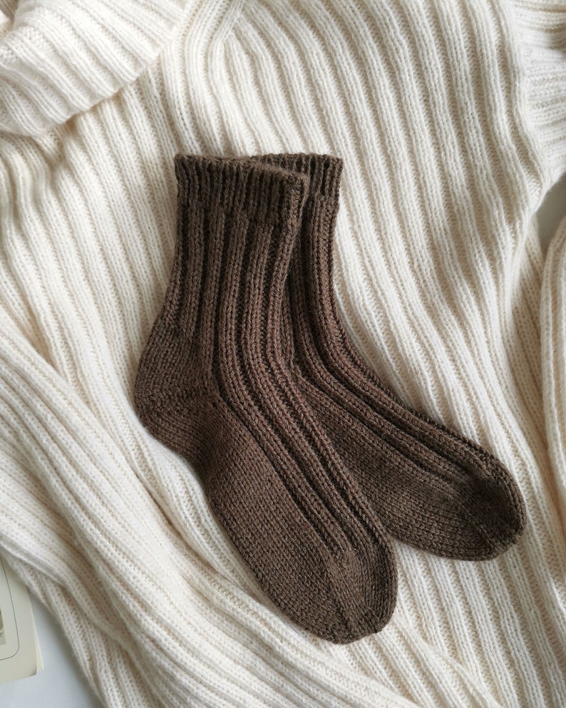 May include: A pair of brown knitted socks on a white knitted sweater. The socks are ribbed and have a simple design.