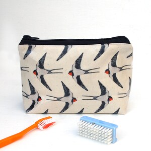 May include: A white zippered pouch with a black zipper and black trim. The pouch has a repeating pattern of black and white swallows with red accents.