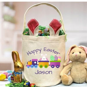 May include: A white canvas Easter basket with bunny ears, featuring a colorful train design and the text "Happy Easter Jason".