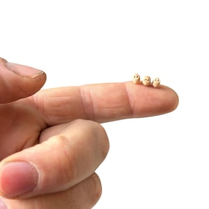 May include: Four tiny ceramic owls lined up on a finger. The owls are beige with brown eyes and beaks.