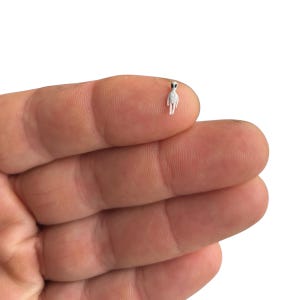 May include: A small white figurine of a person with black eyes. The figurine is standing on a finger.