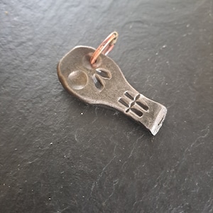 Pode incluir: Um chaveiro de prata em forma de caveira com um anel de cobre. A caveira tem um design detalhado com um pequeno círculo no centro da testa e um design em forma de cruz na parte inferior.