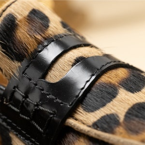 May include: Close-up of a leopard print loafer with black leather straps. The straps have stitching around the edges.