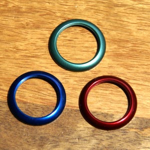 May include: Three metallic rings in blue, green, and red, each with a circular shape and a glossy finish. The rings are displayed on a wooden surface, showcasing their vibrant colors and reflective qualities.