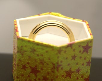 May include: A gold ring with a rounded band sits inside a yellow box with red stars.