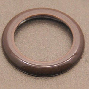 Puede incluir: Un anillo de plástico marrón con un acabado liso y brillante. El anillo tiene una abertura circular en el centro.