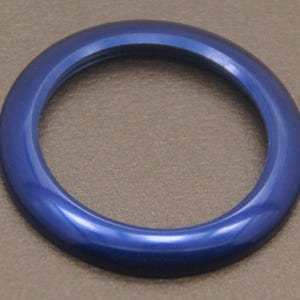 May include: A glossy, deep blue, circular object with a smooth, curved surface. The object has a hollow centre and appears to be made of a solid material. The colour is consistent throughout, with subtle variations in the light.