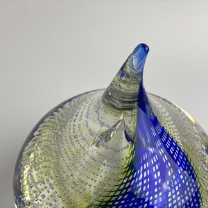 K&ouml;nnte beinhalten: Ein blauer und gr&uuml;ner Glas-Papiergewicht mit einem wirbelnden Design und einer spitzen Spitze. Der Papiergewicht ist mit kleinen Luftblasen gef&uuml;llt.