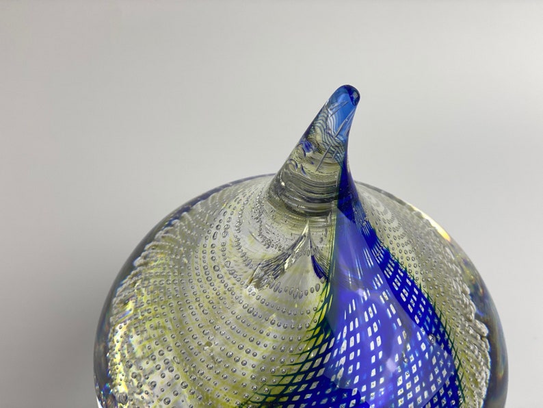 K&ouml;nnte beinhalten: Ein blauer und gr&uuml;ner Glas-Papiergewicht mit einem wirbelnden Design und einer spitzen Spitze. Der Papiergewicht ist mit kleinen Luftblasen gef&uuml;llt.