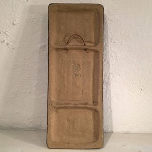 Puede incluir: Una baldosa rectangular de cer&aacute;mica con un esmalte marr&oacute;n. La baldosa tiene dos secciones rectangulares separadas por un borde elevado. La baldosa tiene un gancho de metal en la parte superior y una peque&ntilde;a inscripci&oacute;n que dice "3817".