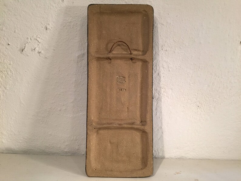 Puede incluir: Una baldosa rectangular de cer&aacute;mica con un esmalte marr&oacute;n. La baldosa tiene dos secciones rectangulares separadas por un borde elevado. La baldosa tiene un gancho de metal en la parte superior y una peque&ntilde;a inscripci&oacute;n que dice "3817".