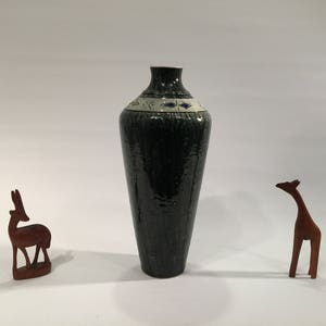 Może przedstawiać: Zielony ceramiczny wazon z białym i niebieskim paskiem z wzorem wok&oacute;ł środka. Wazon stoi na białym tle.