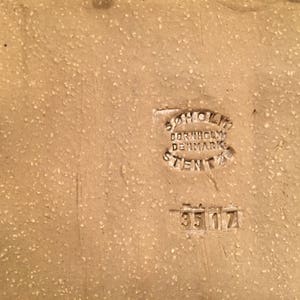Puede incluir: Primer plano de una baldosa de cer&aacute;mica de color tostado con un sello marr&oacute;n que dice "Bornholm Denmark Stengods" y el n&uacute;mero "35 17".
