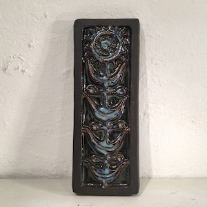 Puede incluir: Un azulejo de cer&aacute;mica marr&oacute;n oscuro con un dise&ntilde;o floral azul y blanco. El azulejo presenta una flor estilizada con un c&iacute;rculo central y cuatro p&eacute;talos. La flor est&aacute; rodeada de cuatro flores estilizadas m&aacute;s peque&ntilde;as.