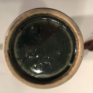 Może przedstawiać: Zbliżenie na sp&oacute;d ceramicznego wazonu z ciemnozieloną glazurą. Sp&oacute;d jest oznaczony czarnym atramentem, na kt&oacute;rym widnieje napis "29 kwietnia 1941".