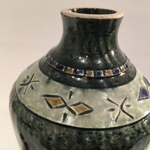 Może przedstawiać: Zielony ceramiczny wazon z białym pasem wok&oacute;ł środka. Pas ma geometryczny wz&oacute;r w kolorze brązowym i niebieskim. Wazon ma wąską szyjkę i szeroką podstawę.