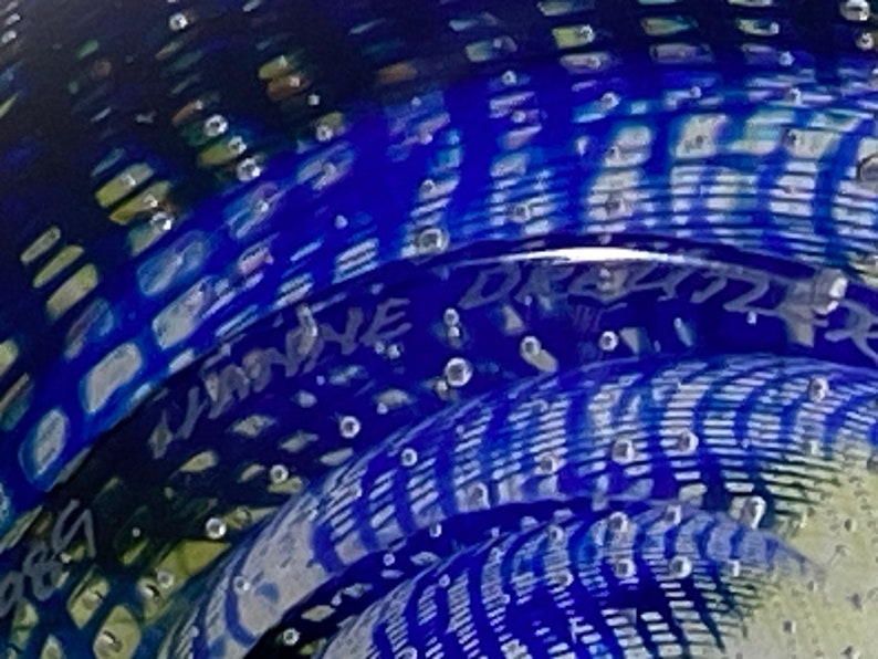 K&ouml;nnte beinhalten: Ein blauer Glas-Briefbeschwerer mit einem wirbelnden Muster und Luftblasen. Der Briefbeschwerer ist signiert mit "Limoine" und "Dreizler".