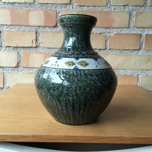 Może przedstawiać: Zielony ceramiczny wazon z geometrycznym wzorem w kolorze białym, niebieskim i złotym. Wazon ma fakturowaną powierzchnię i zaokrąglony korpus.