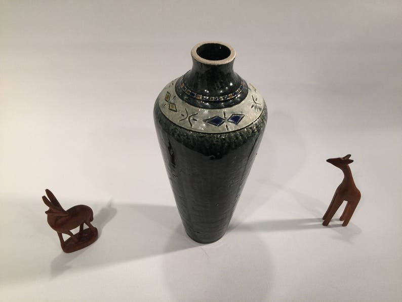 Może przedstawiać: Zielony ceramiczny wazon z białym i niebieskim geometrycznym wzorem wok&oacute;ł g&oacute;rnej części. Wazon stoi na białym tle.