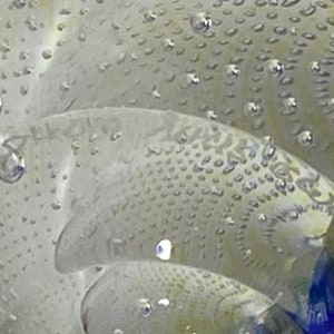 K&ouml;nnte beinhalten: Nahaufnahme eines durchsichtigen Glas-Papiergewichts mit einer strukturierten Oberfl&auml;che und kleinen Luftblasen, die darin eingeschlossen sind. Das Glas hat ein blaues und wei&szlig;es Spiralmuster.