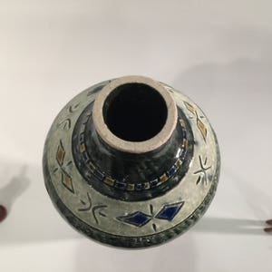 Może przedstawiać: Ceramiczny wazon z geometrycznym wzorem w kolorze niebieskim, białym i złotym. Wazon ma szeroki otw&oacute;r i wąską szyjkę.