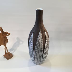 Puede incluir: Un jarrón de cerámica marrón y blanco con un patrón geométrico. El jarrón tiene un cuello estrecho y una base ancha y redondeada.