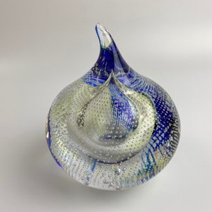 K&ouml;nnte beinhalten: Ein durchsichtiger Glas-Papiergewicht mit blauen und wei&szlig;en Wirbeln und Luftblasen. Der Papiergewicht hat eine spitze Oberseite und eine abgerundete Basis.