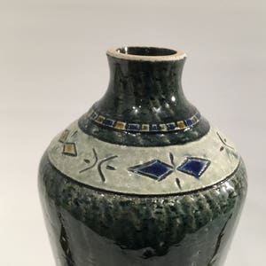 Może przedstawiać: Zielony ceramiczny wazon z białym paskiem i niebieskimi i złotymi geometrycznymi wzorami.
