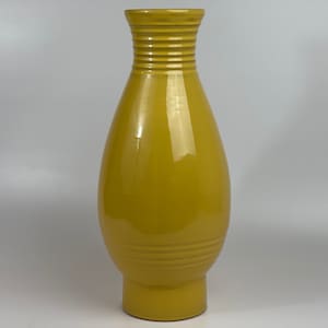 Könnte beinhalten: Eine hohe, gelbe Keramikvase mit rundem Körper und einem ausgestellten oberen Rand. Die Vase hat eine glänzende Oberfläche und ein geripptes Design.
