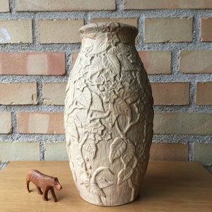May include: A white ceramic vase with an embossed floral design. The vase is tall and slender with a rounded base and a narrow opening.