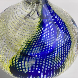 K&ouml;nnte beinhalten: Eine klare Glasvase mit einem geometrischen Muster in Blau, Gr&uuml;n und Gelb. Die Vase hat eine strukturierte Oberfl&auml;che mit kleinen Blasen.
