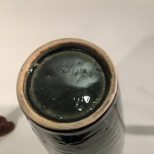 Może przedstawiać: Zielony ceramiczny wazon z jasnobrązową krawędzią. Na spodzie wazonu znajduje się podpis odręczny, kt&oacute;ry brzmi "IBF".