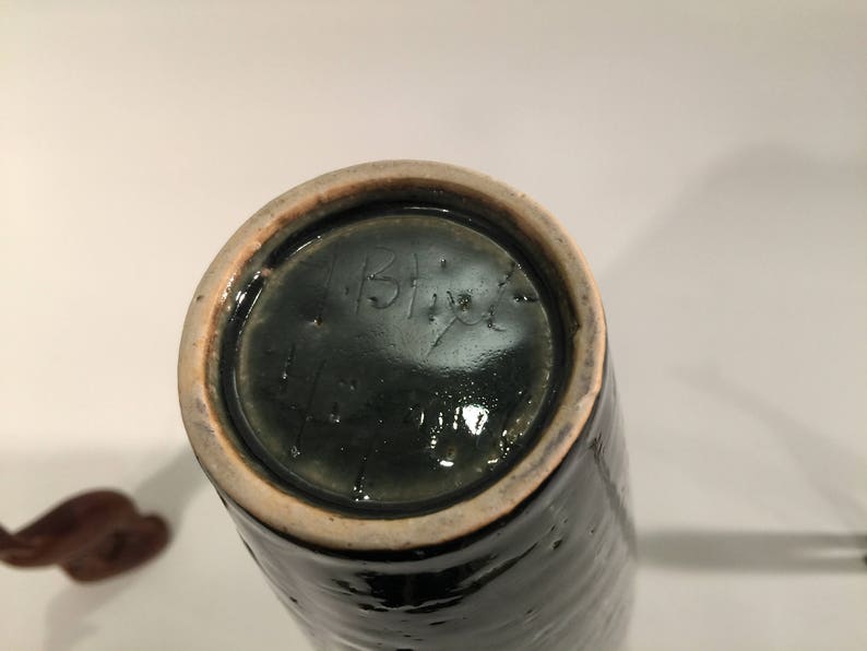 Może przedstawiać: Zielony ceramiczny wazon z jasnobrązową krawędzią. Na spodzie wazonu znajduje się podpis odręczny, kt&oacute;ry brzmi "IBF".