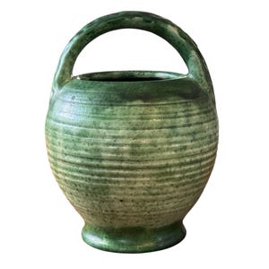 May include: A green ceramic vase with a wide mouth and a rounded body. The vase has a single handle and a textured surface.