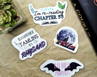 Puede incluir: Cuatro pegatinas diferentes con citas del libro A Court of Thorns and Roses. Las pegatinas están sobre una superficie marrón. La primera pegatina dice "Im re-reading CHAPTER 55" con un libro y corazones. La segunda pegatina dice "In a world full of TAMLINS be a RHYSAND" con una espada y estrellas. La tercera pegatina dice "Light it up" con una luna y alas. La cuarta pegatina dice "BAT BOYS PROPERTY" con un murciélago negro.