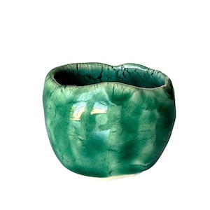 May include: A small, green ceramic bowl with an irregular, slightly wavy rim. The bowl has a textured, crackled glaze.