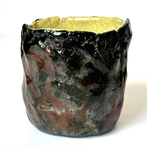 May include: A small, dark green ceramic planter with a textured surface and a yellow glaze on the rim. The planter has a rustic, handmade look.